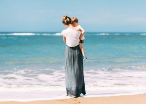 Mutter trägt ihr Kind am Strand und blickt aufs Meer, Sinnbild für verbundene Familienberatung in Buchholz in der Nordheide