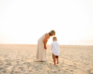Mutter beugt sich liebevoll über Kind am Strand