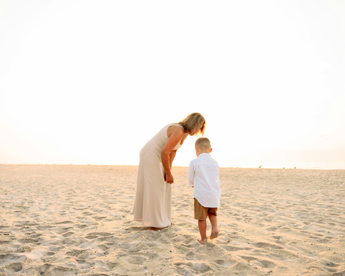 Mutter beugt sich liebevoll über Kind am Strand
