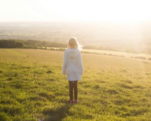 Kind steht allein auf einer Wiese im warmen Abendlicht, Thema Loben und Selbstvertrauen im Familiencoaching Hamburg