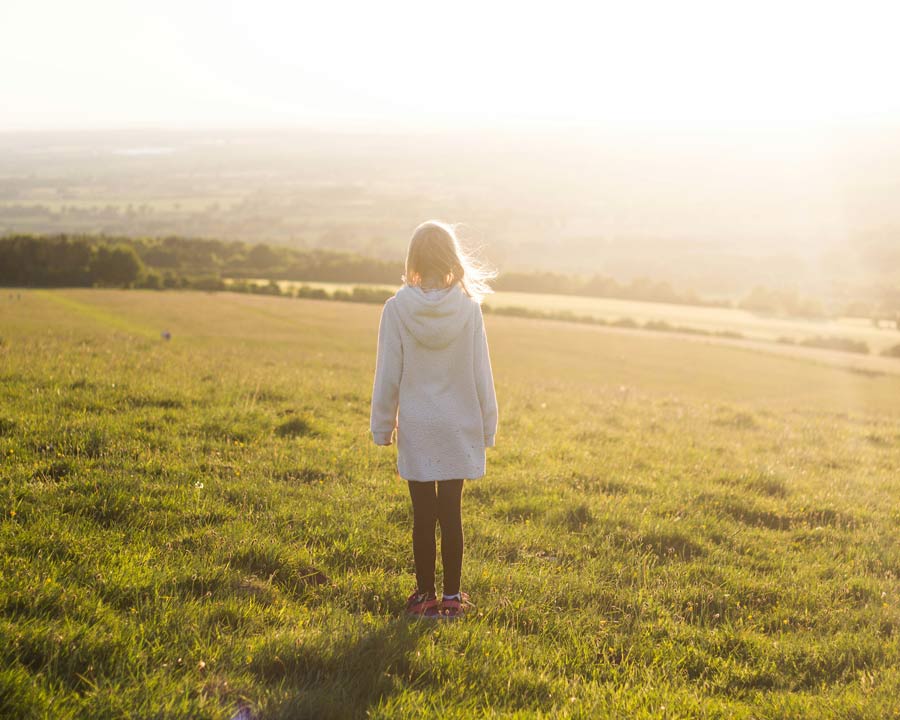 Kind steht allein auf einer Wiese im warmen Abendlicht, Thema Loben und Selbstvertrauen im Familiencoaching Hamburg