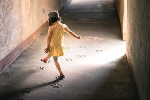 Kleines Kind im gelben Kleid geht auf einen hellen Lichtstrahl zu, Thema Hauen mit zwei Jahren und Familiencoaching Hamburg