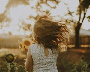 Kleines Mädchen mit wehenden Haaren vor Sonnenblumen im Gegenlicht, Thema schreiendes Kind und Erziehungsberatung Hamburg