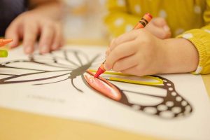 Kinderhand malt mit Buntstiften einen Schmetterling aus, Thema Kindergarten und Elternberatung Hamburg